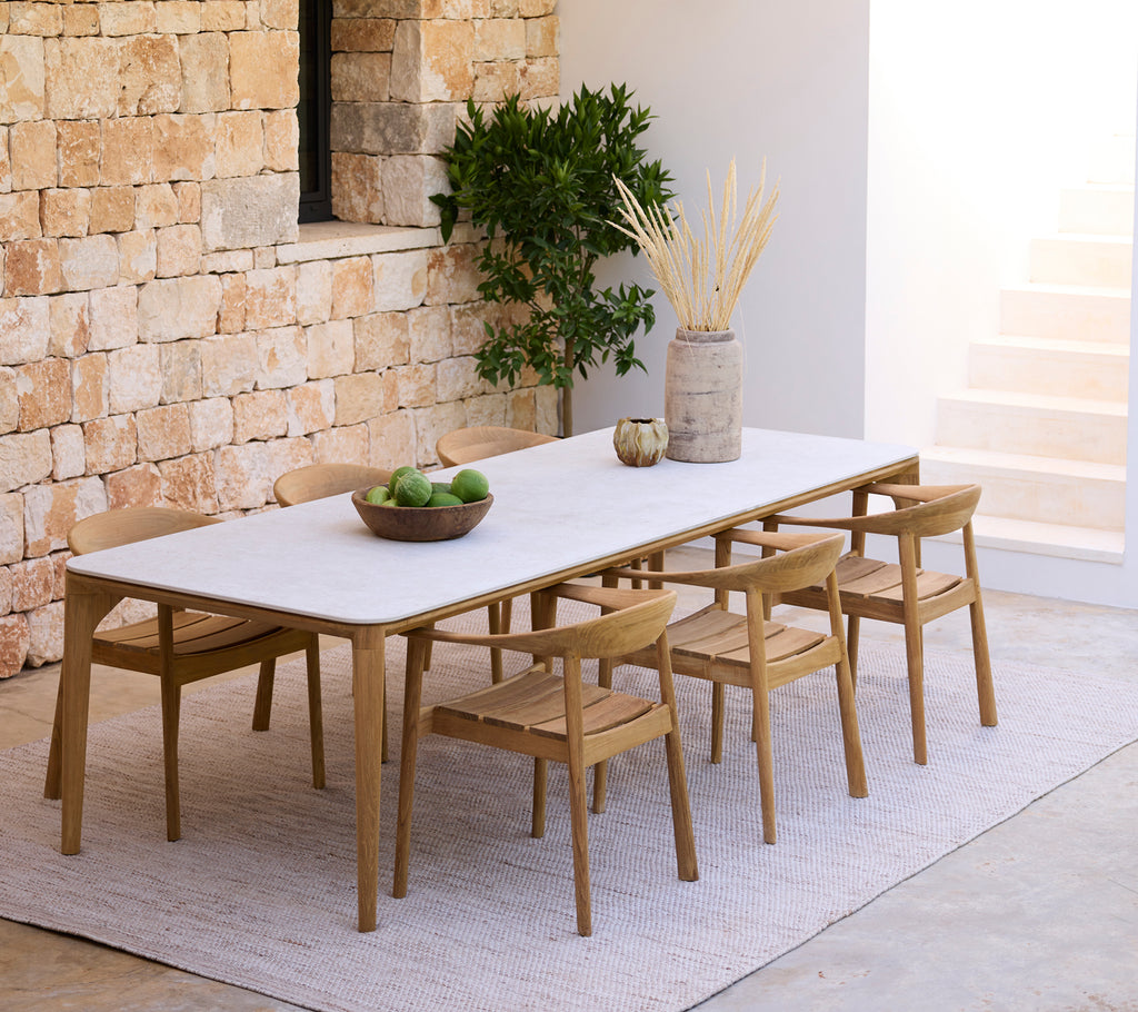 Configuración moderna de comedor con una mesa blanca y sillas de madera contra una pared de piedra.