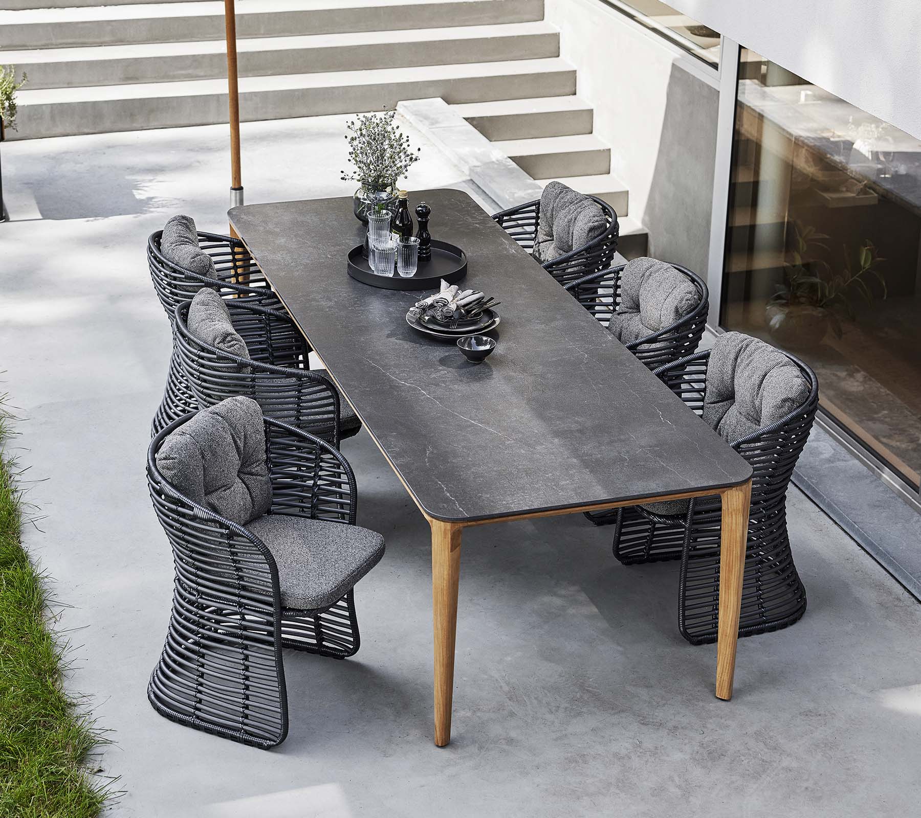 Sillas de mimbre rodean una mesa elegante, complementada por una sombrilla clásica y centros de mesa decorativos para una invitante disposición de comedor al aire libre.