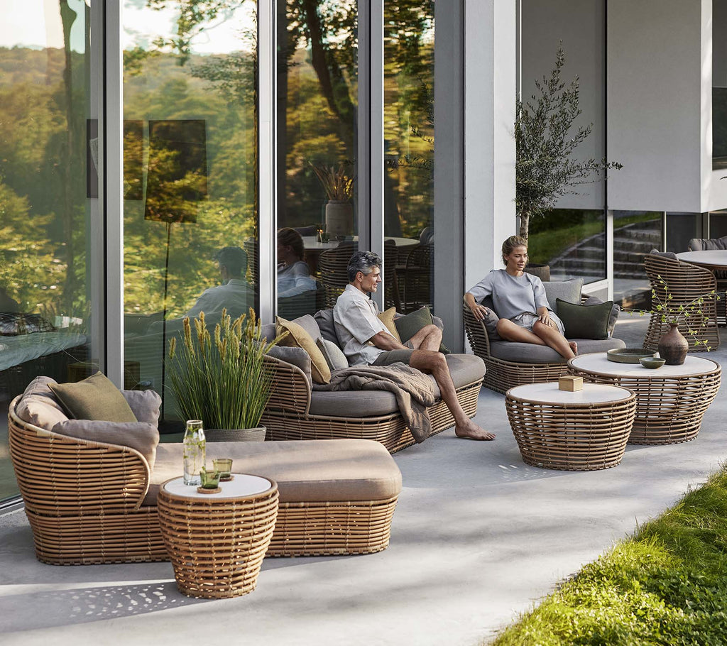 Area de estar elegante con una cama solar de mimbre, una silla lounge y una mesa de café con elementos naturales, creando una atmósfera acogedora y relajante.