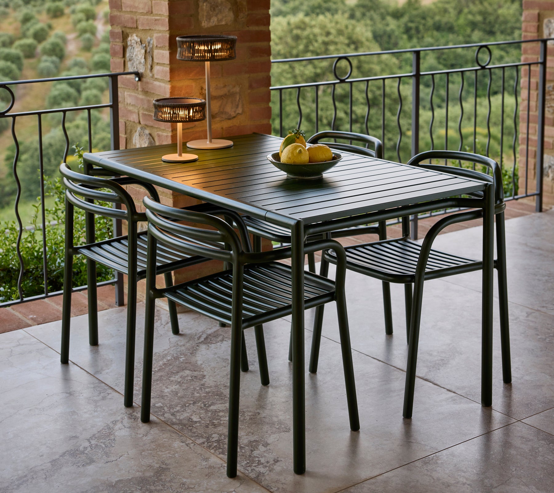 Un conjunto de comedor elegante que incluye una mesa elegante, cuatro sillas y una lámpara elegante, complementado con un bol de frutas decorativo.