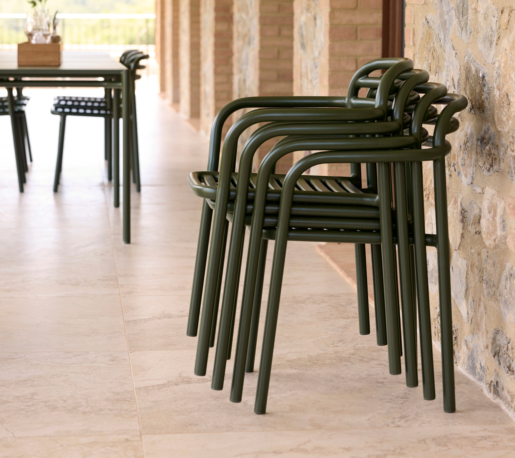 Sillas Bliss apiladas en un entorno al aire libre, con un diseño elegante y un color verde tierra contra una pared de piedra.