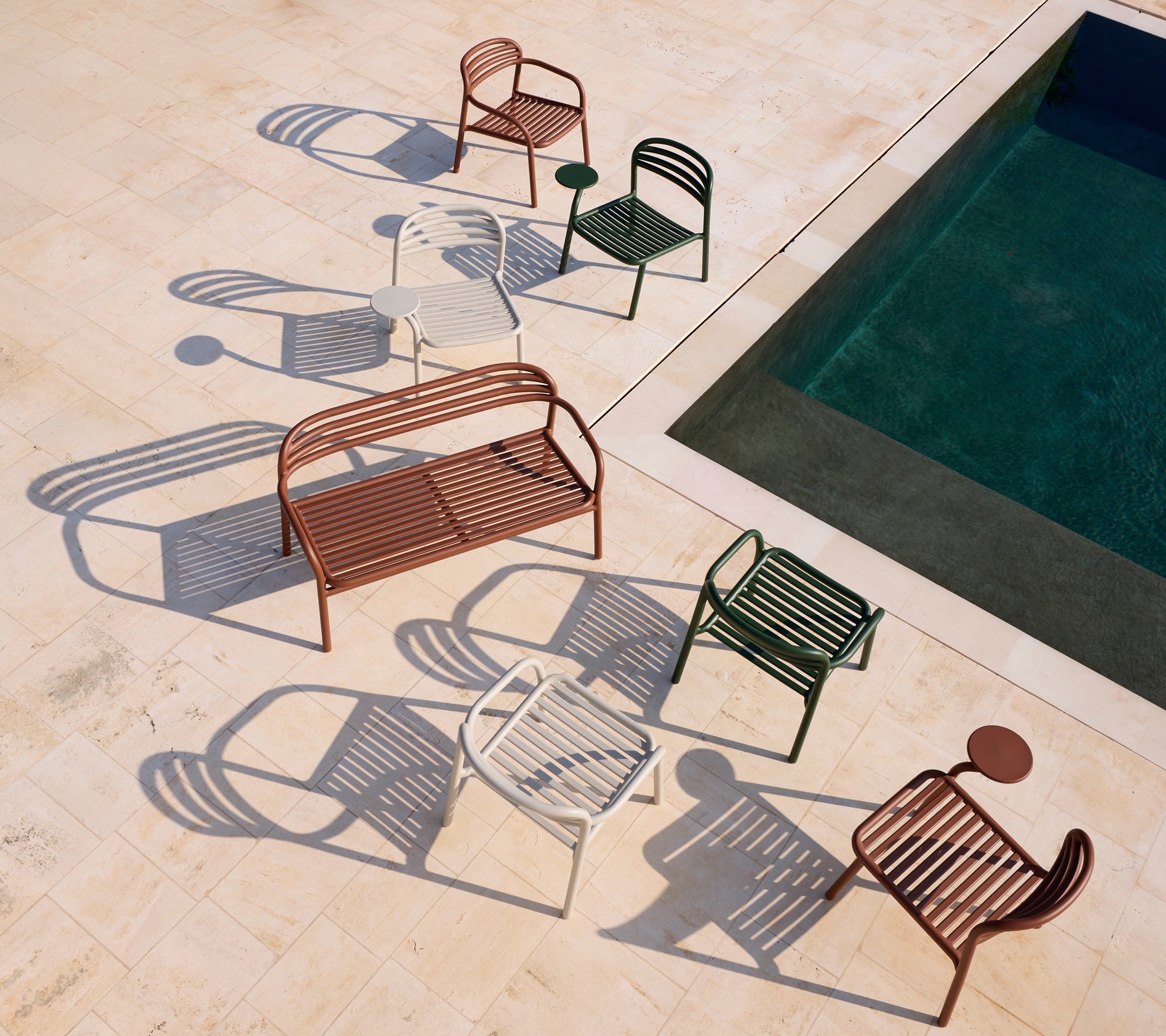 Conjunto de sillas modernas rojas, blancas, verdes y un banco marrón cerca de una piscina.