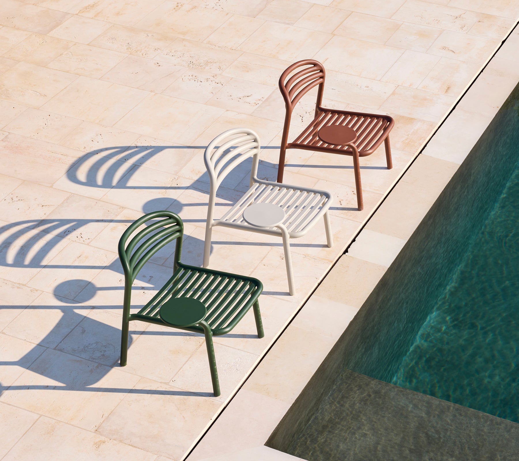 Tres sillas modernas en verde, blanco y marrón al lado de una piscina.