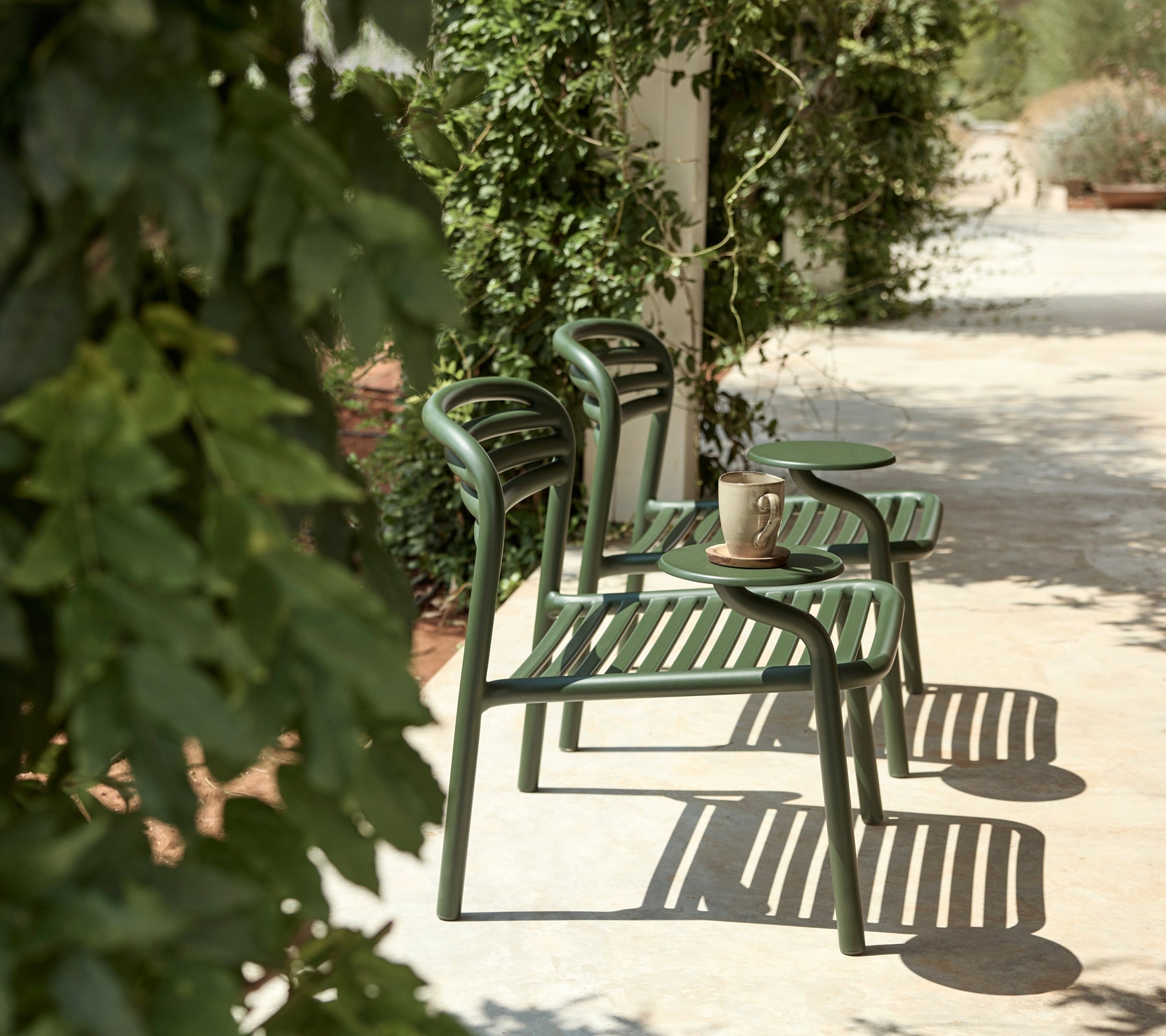 Sillas verdes y mesa auxiliar en un entorno al aire libre con abundante vegetación.