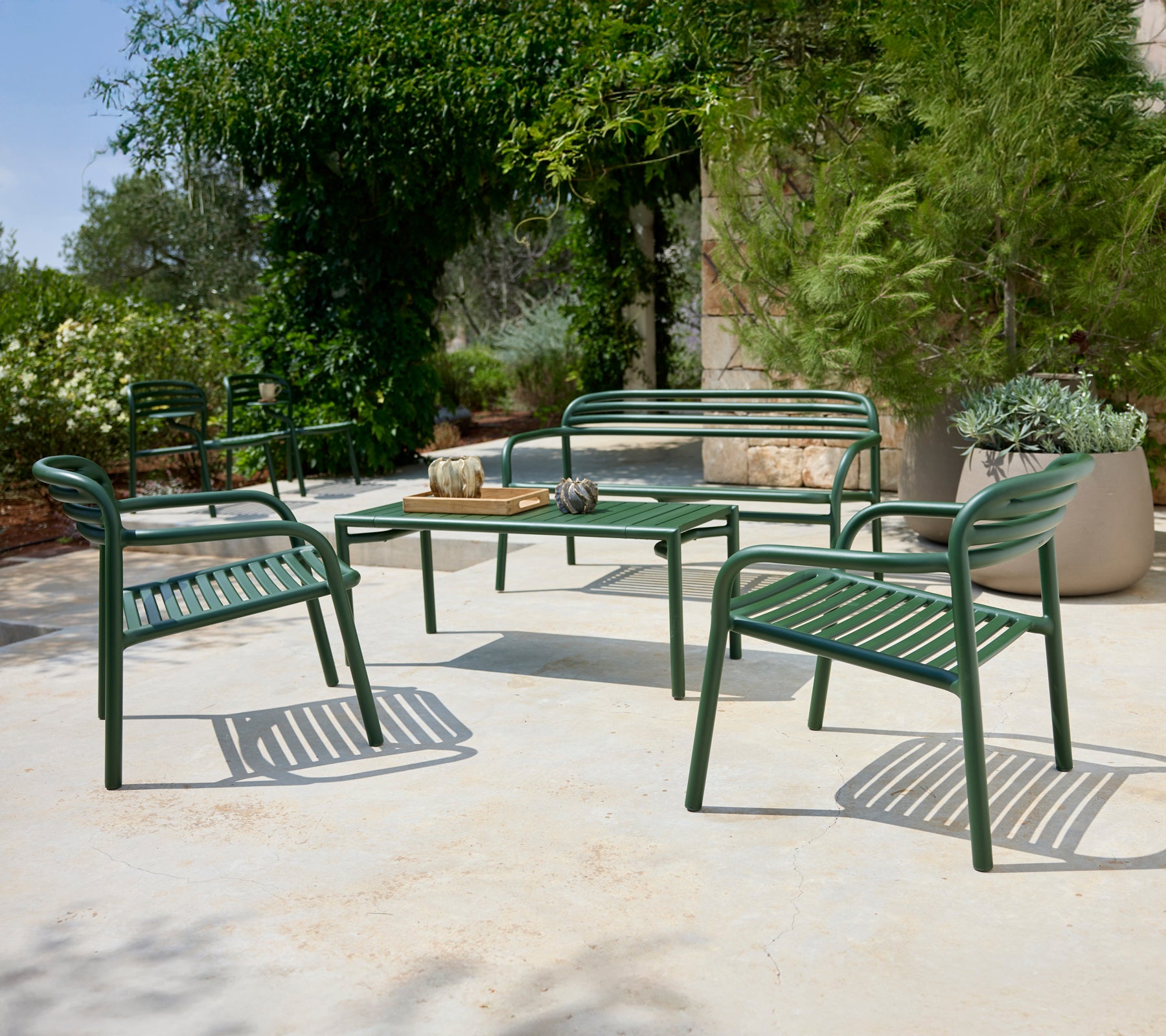 Disposición de asientos exteriores verdes con sillas y un banco alrededor de una mesa.