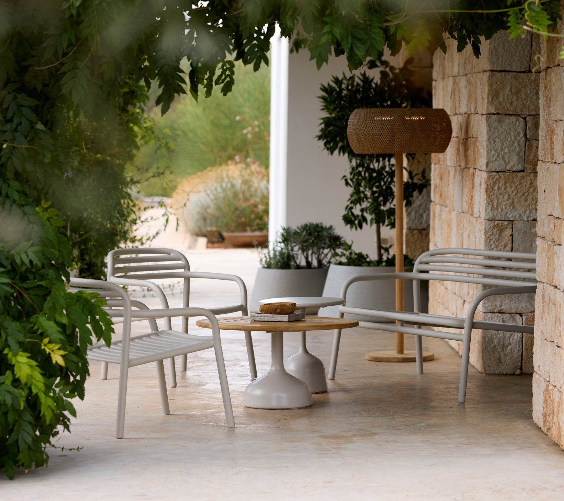 Sillas de salón gris modernas y una mesa blanca al lado de una lámpara de madera en un entorno exterior sereno.
