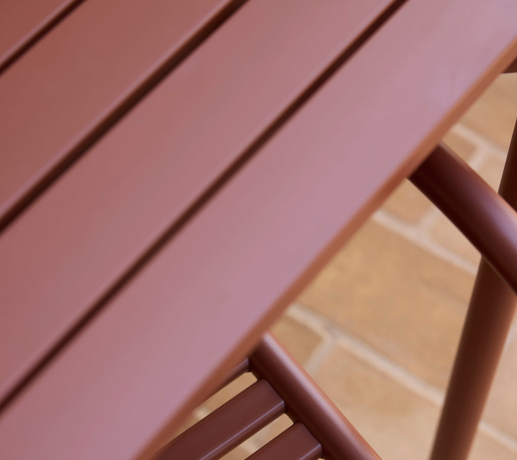 Una vista en primer plano de una mesa Bliss roja desértica que muestra su superficie lisa y su diseño elegante.