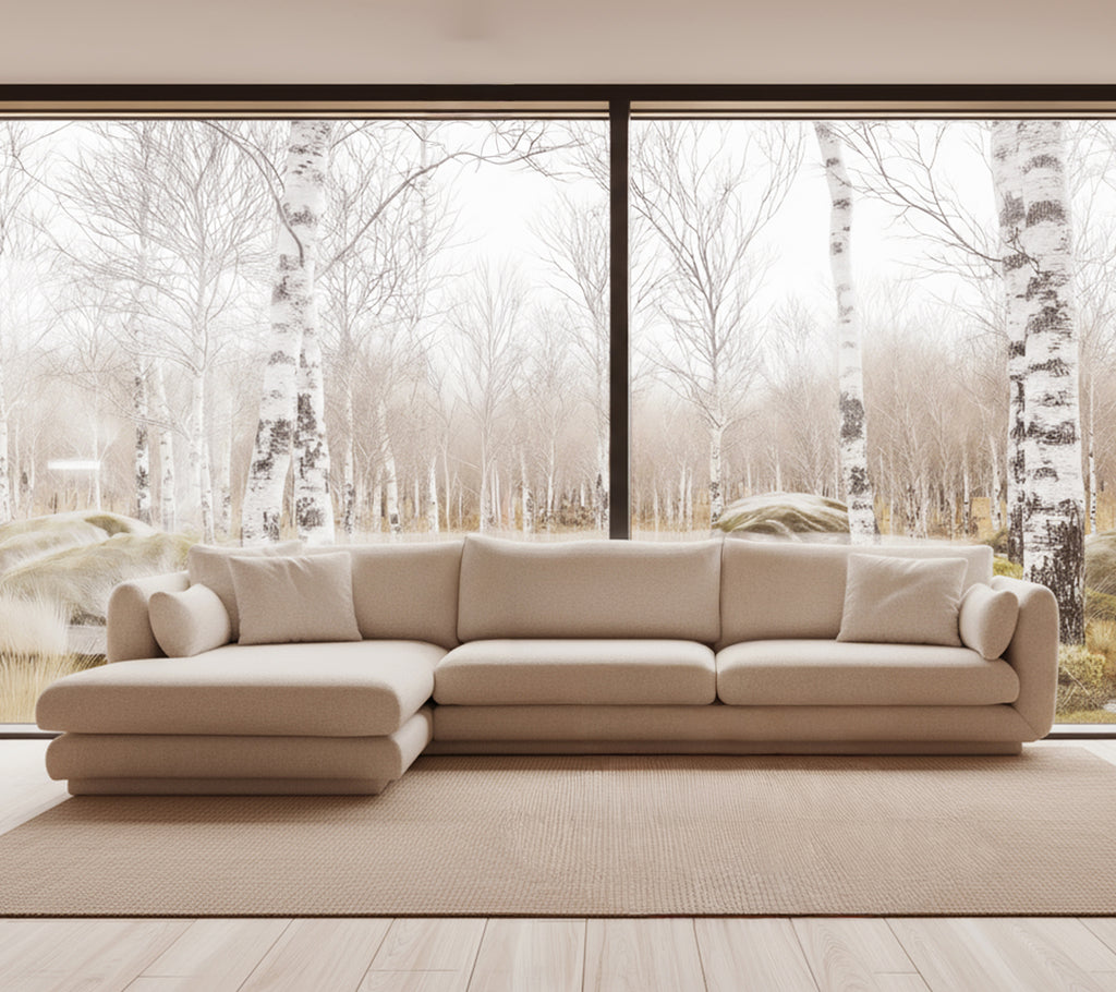 Sofá moderno beige en un entorno de salón brillante con grandes ventanas.
