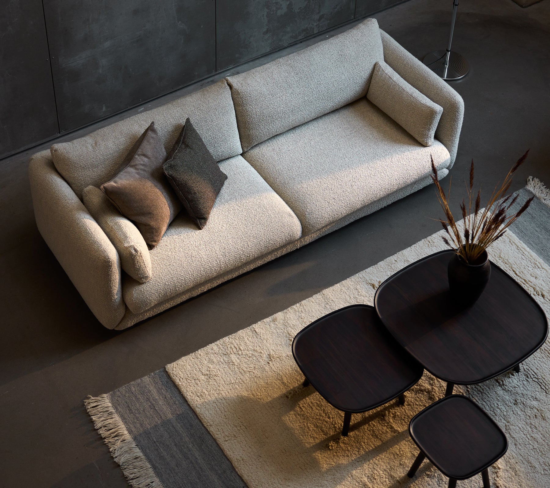 Sofá de tres plazas elegante en color arena, complementado con tres tamaños de mesas de café negras elegantes y almohadas decorativas.