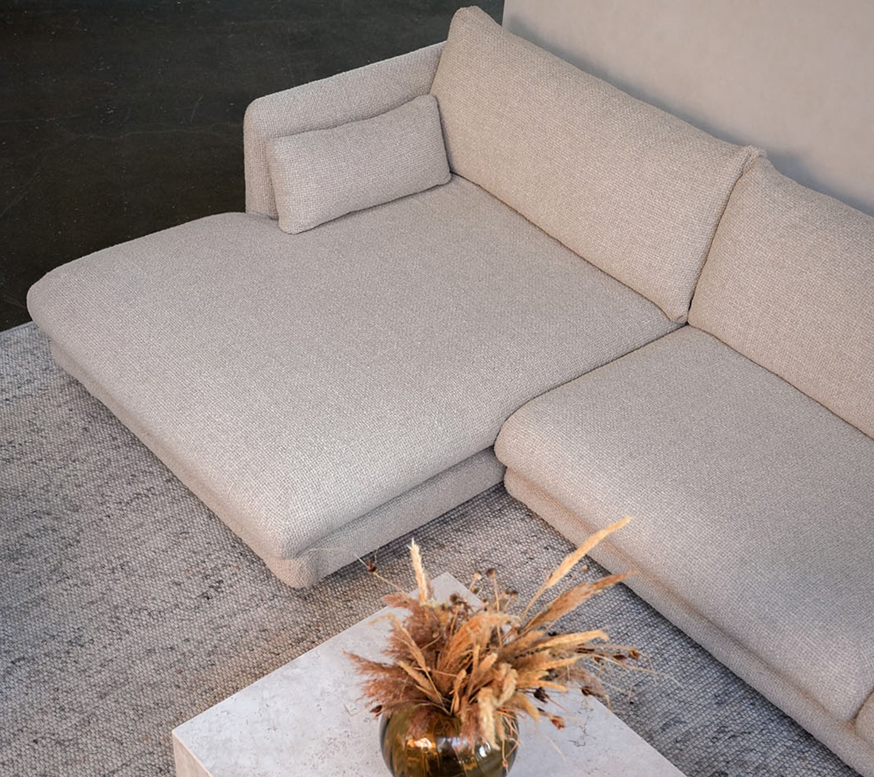 Sofá beige moderno con una mesa blanca y un jarrón decorativo en un entorno elegante de salón.