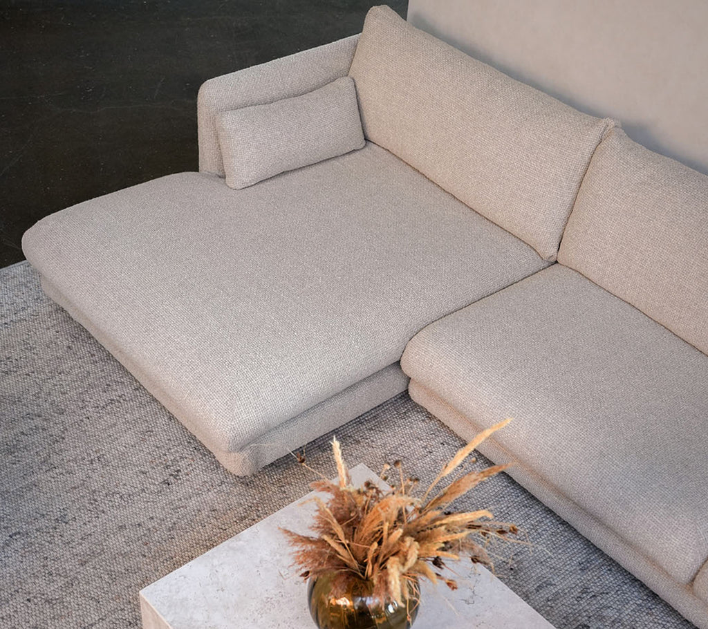 Sofá beige moderno con una mesa blanca y un jarrón decorativo en un entorno elegante de salón.