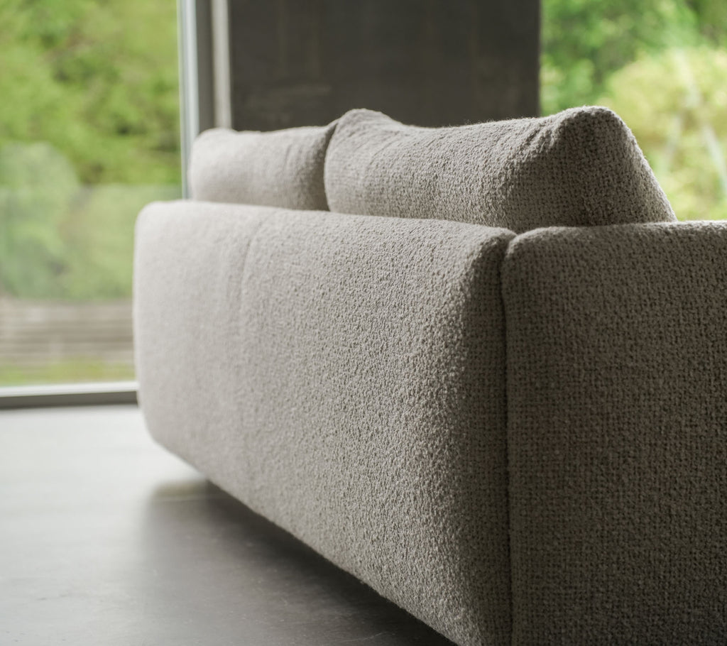 Sofá contemporáneo con un tejido texturizado de color arena, acentuado por elegantes patas de teca, que muestra el estilo de Cane-line y cojines suaves.