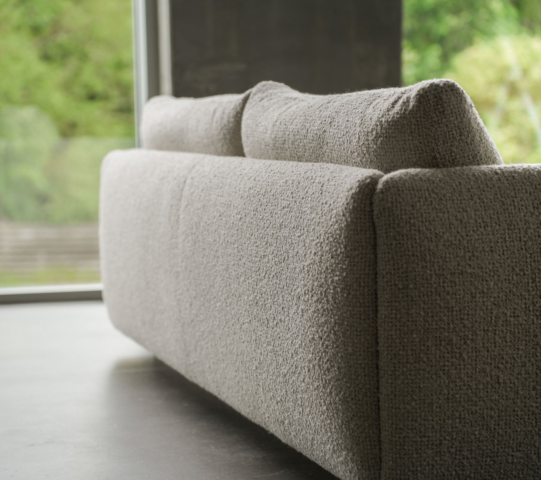 Sofá contemporáneo con un tejido texturizado de color arena, acentuado por elegantes patas de teca, que muestra el estilo de Cane-line y cojines suaves.