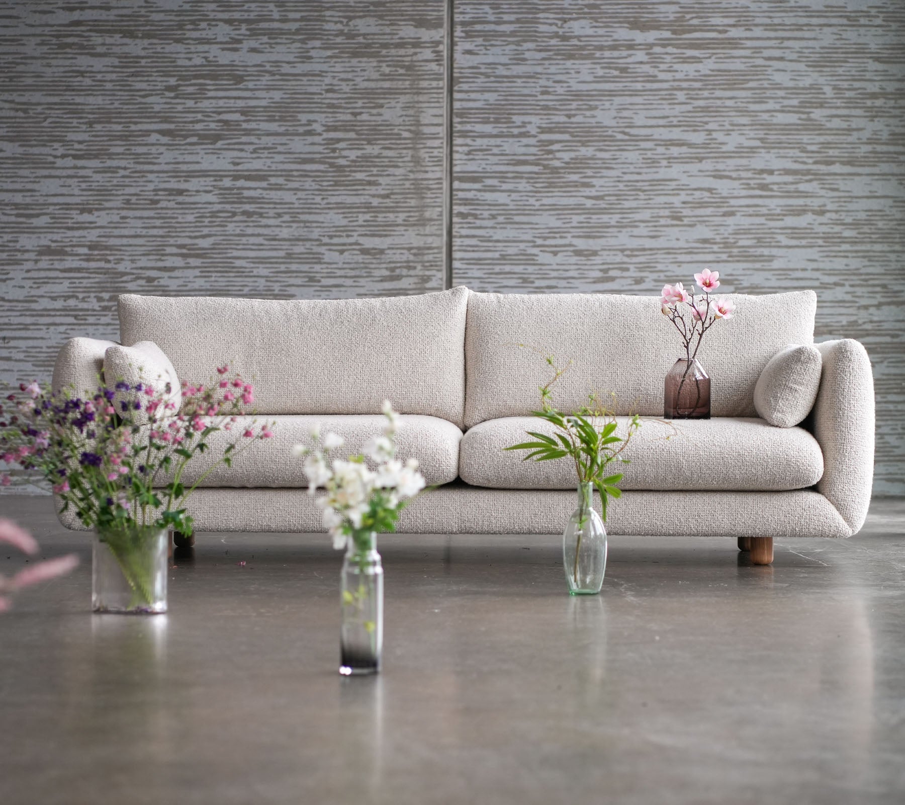 Un sofá de color claro con patas de teca, rodeado de jarrones de flores, que muestra una mezcla de elegancia y estilo Cane-line.