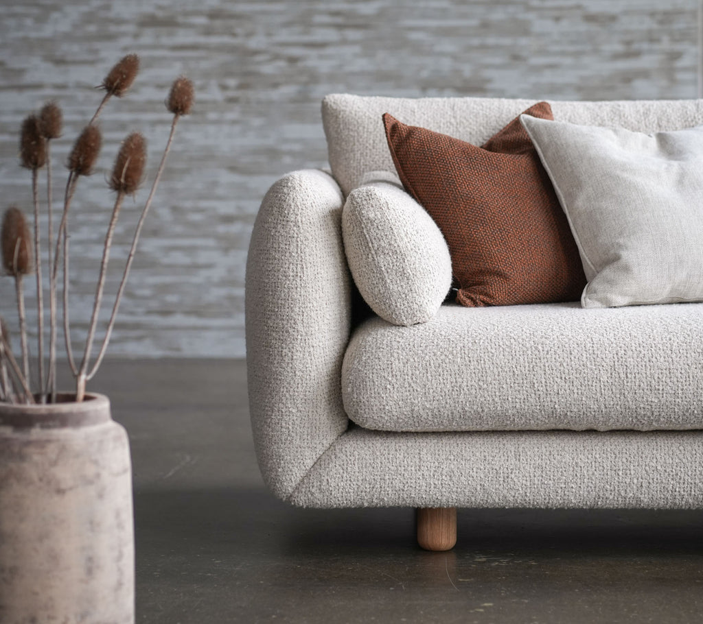 Sofá acogedor con tapicería de flores, patas de teca y cojines elevados, acompañado de un jarrón decorativo y flores secas. Diseño elegante y acogedor.