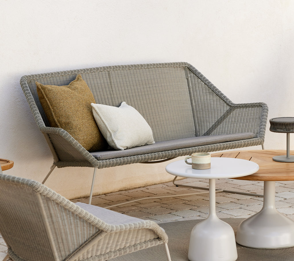Zona de lounge moderna con un sofá gris con cojines y mesas redondas.
