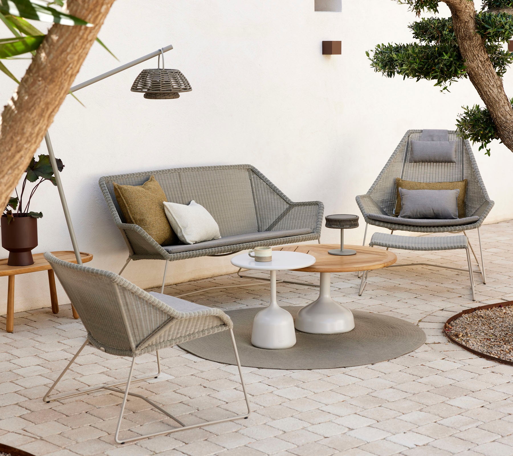 Asientos de lounge elegantes con una mesa de café, con cojines texturizados y tonos naturales, rodeados de vegetación y una iluminación suave.
