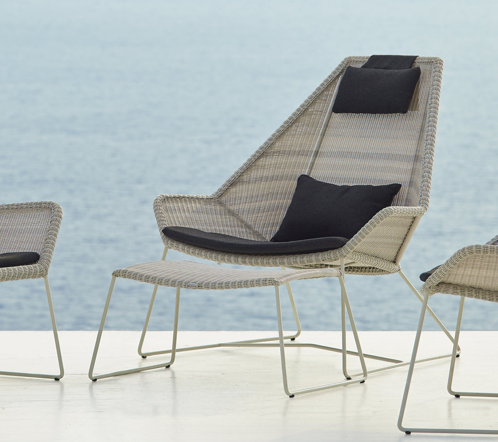 Silla tejida moderna con un cojín negro junto al agua.