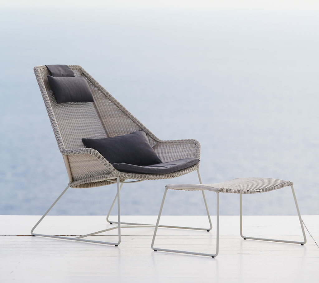 Silla gris moderna con cojín negro y otomana gris frente a un fondo pintoresco.