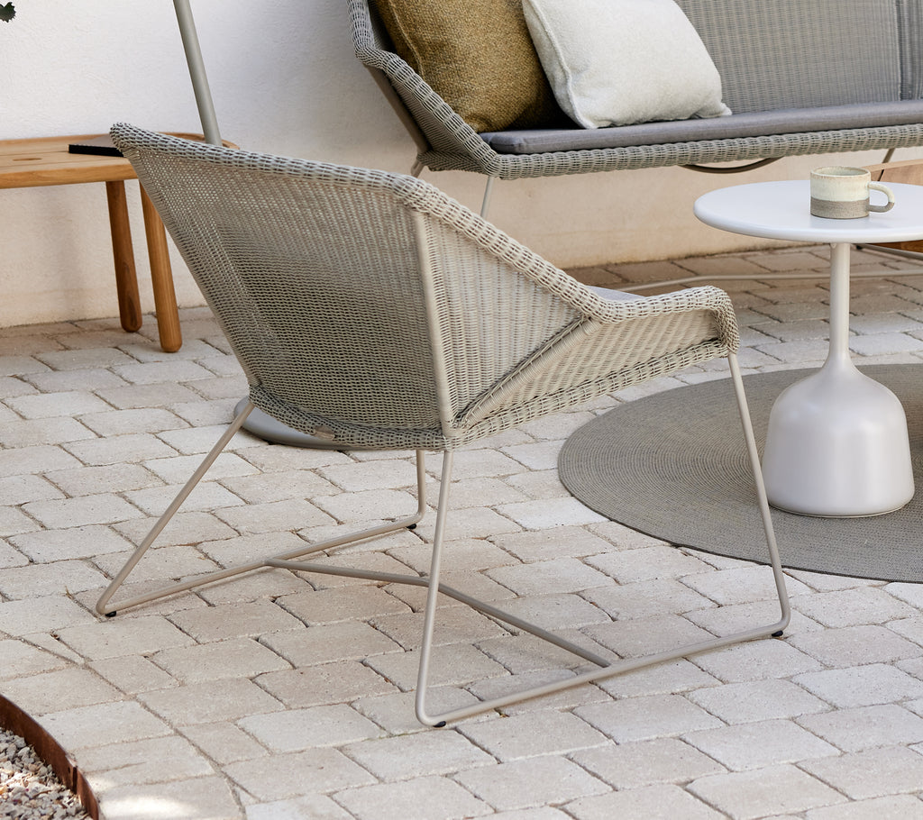 Silla lounge gris con mesa lateral blanca en un entorno exterior moderno.