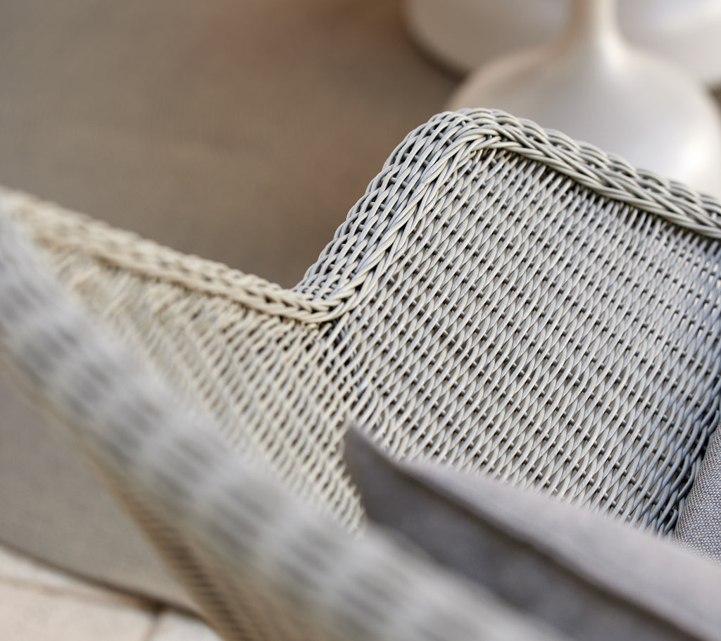 Sillón de mimbre gris con un cojín gris.
