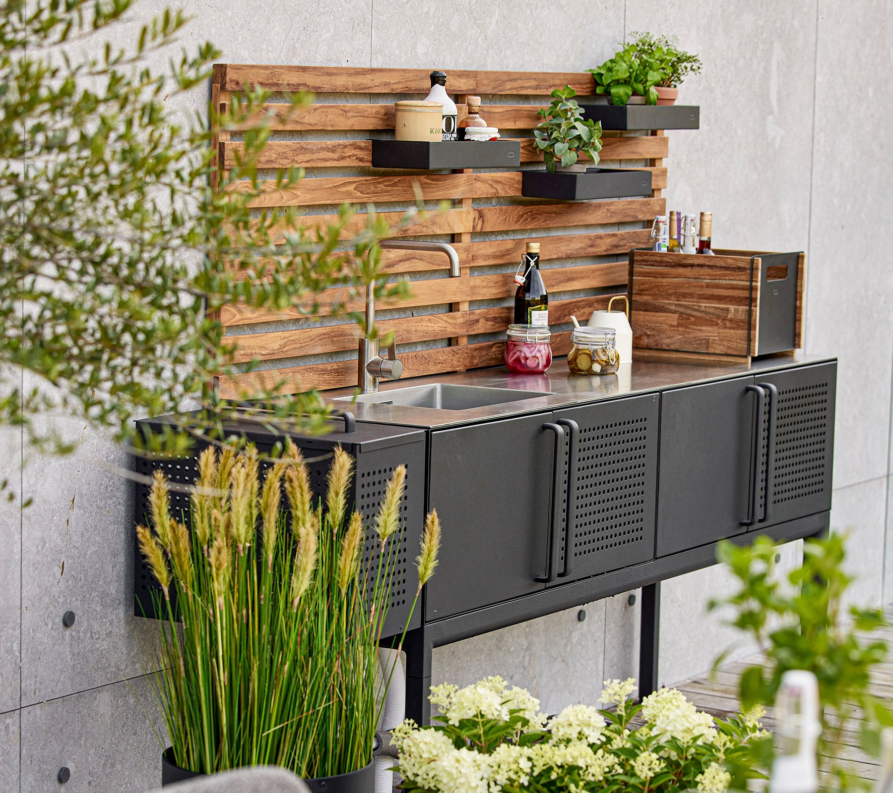 Unidad de cocina negra moderna con un fregadero, estanterías de madera y varias plantas, creando un espacio de trabajo elegante y funcional.