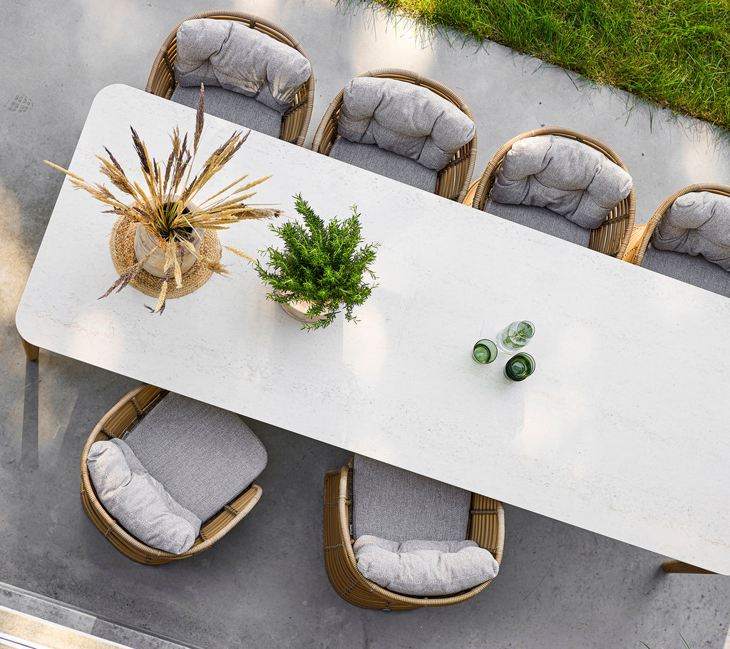 Una larga y elegante mesa rodeada de sillas elegantes, adornada con una planta decorativa y botellas de vidrio en la parte superior.