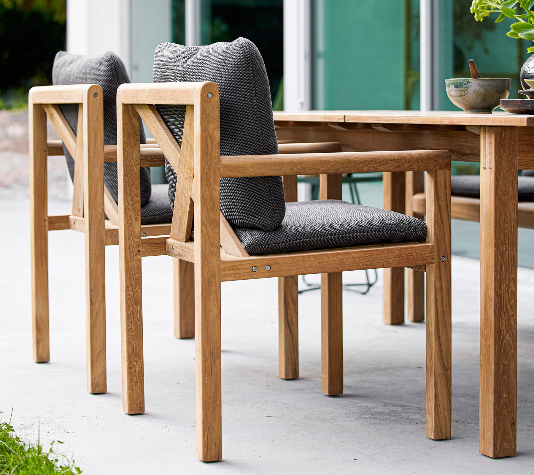 Sillas de madera con asientos acolchados grises, diseñadas para la comodidad, que complementan una mesa de madera en un entorno elegante.