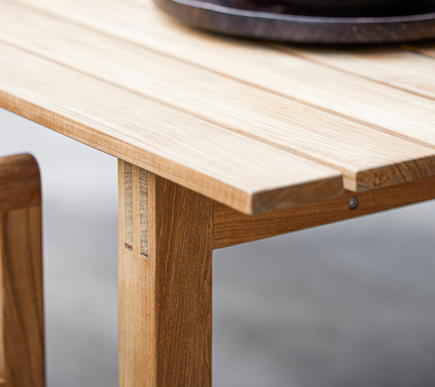 Primer plano de una mesa de madera que muestra un diseño de listones y un tazón decorativo redondo oscuro en la parte superior. Perfecto para una estética de comedor moderno.