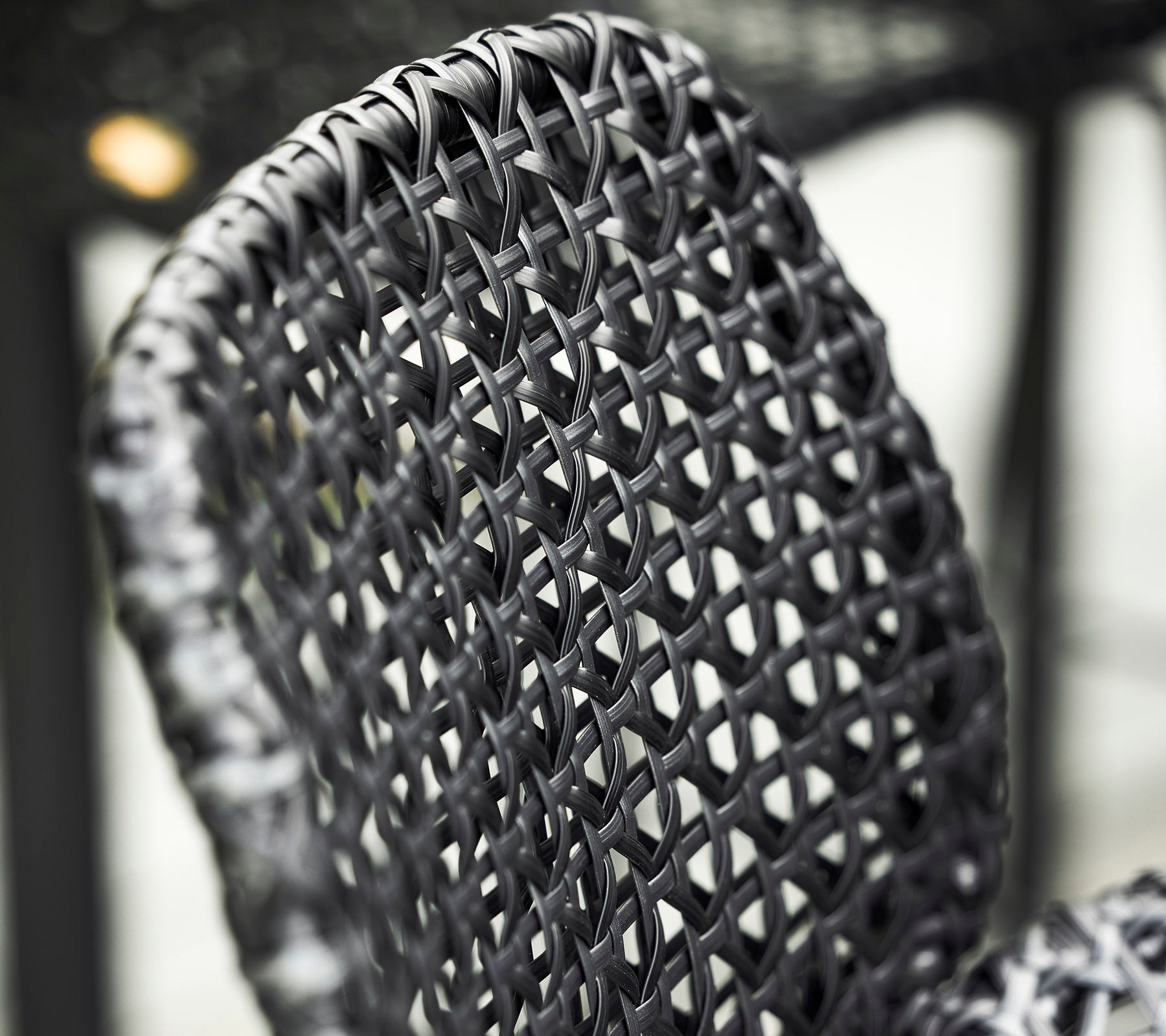 Primer plano de un respaldo de silla tejido en negro, que muestra patrones y texturas intrincados en su diseño.