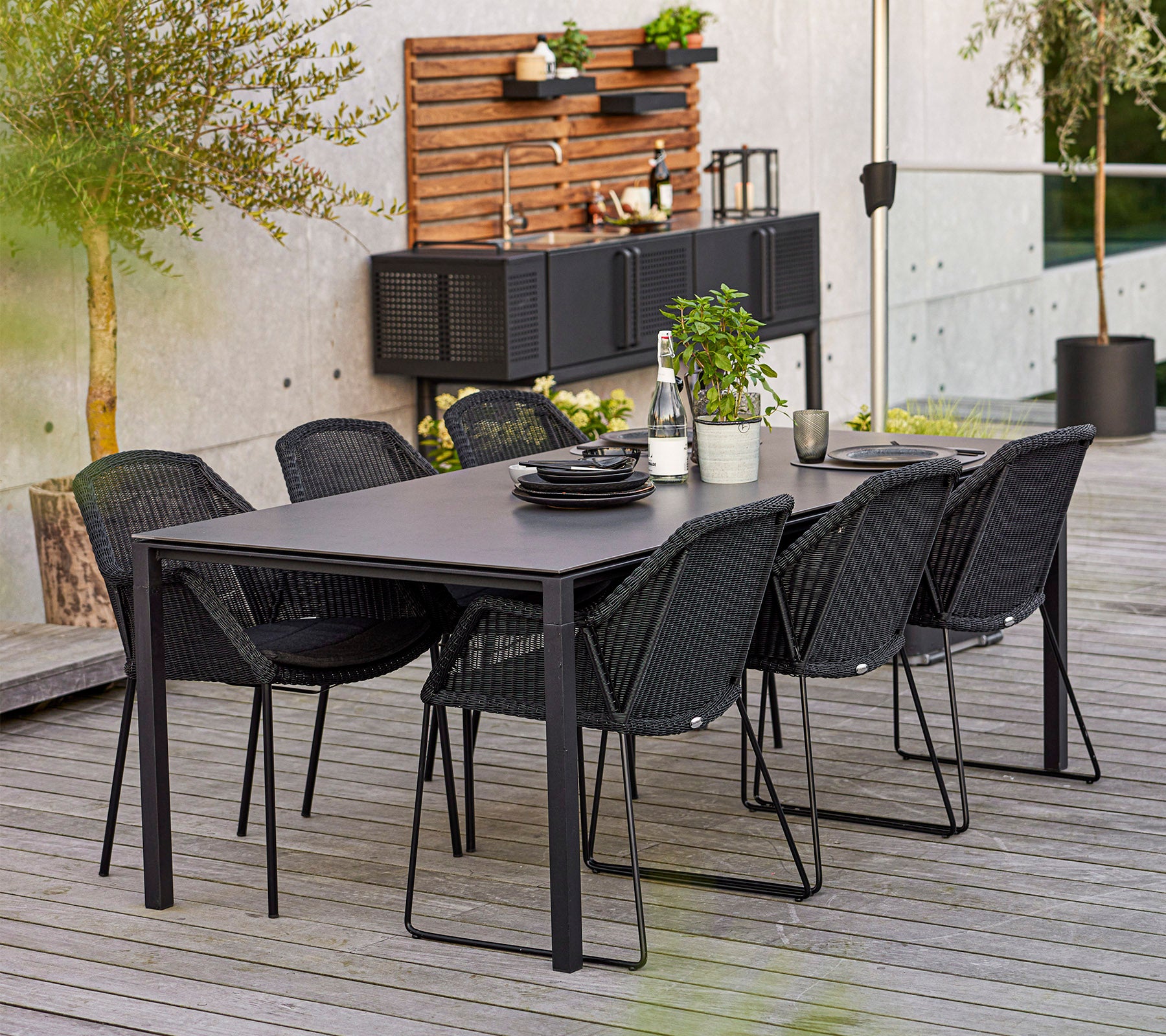Un juego de comedor moderno con una mesa rectangular y seis sillas elegantes, complementado con plantas decorativas y vajilla.