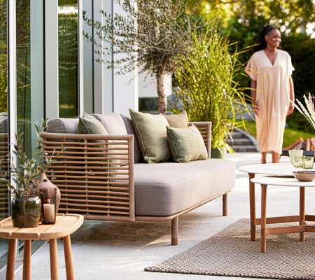 Una área de estar acogedora con un sofá claro, cojines verdes, plantas decorativas y una mesa de madera, creando una atmósfera invitante.