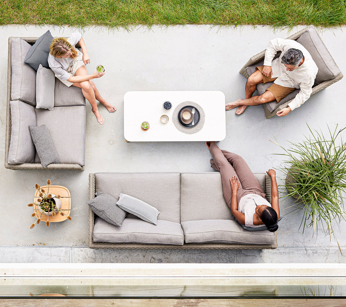 Tres personas se relajan en elegantes asientos gris claro alrededor de una mesa de café minimalista, disfrutando de bebidas y conversación en un entorno sereno.