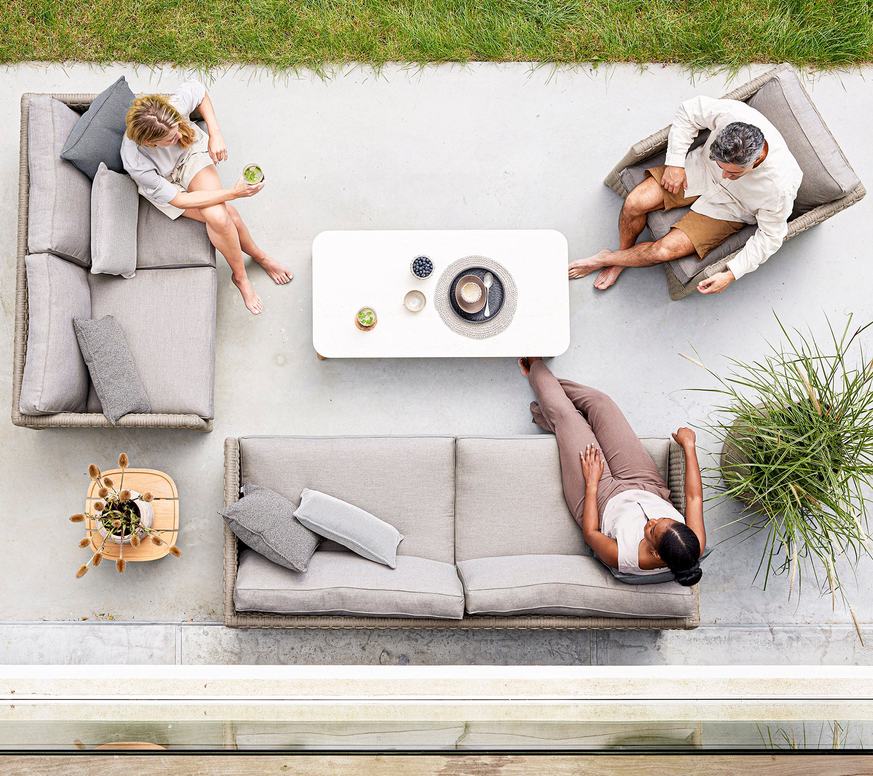 Tres personas se relajan en elegantes asientos gris claro alrededor de una mesa de café minimalista, disfrutando de bebidas y conversación en un entorno sereno.