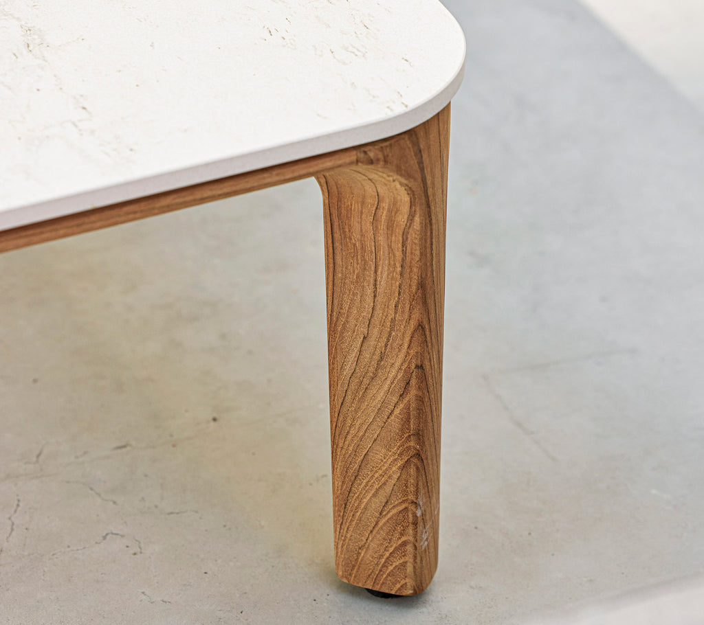 Un primer plano de una mesa con una pierna de madera texturizada y una superficie blanca y lisa. Se destacan elementos de diseño elegantes y modernos.