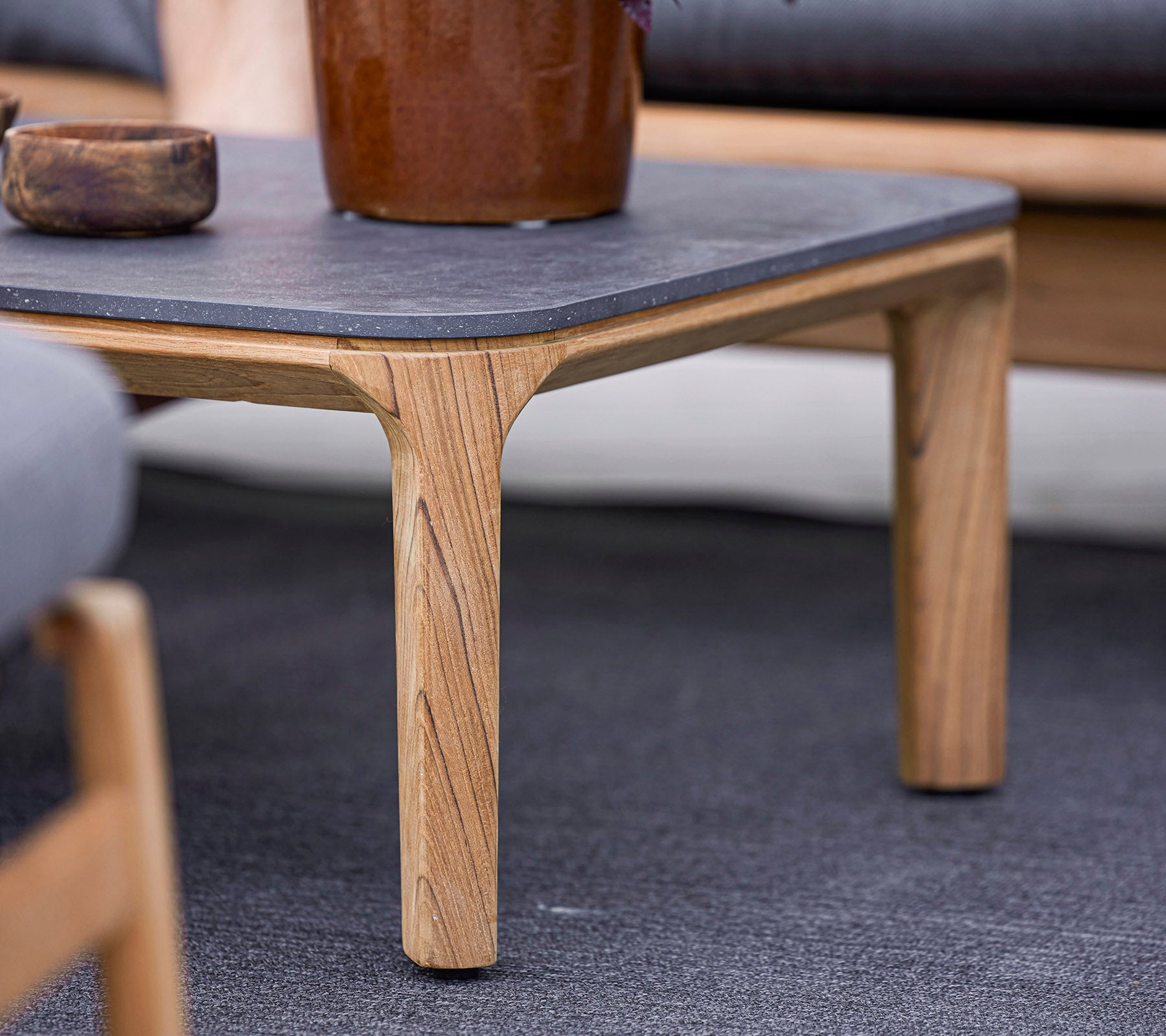 Una mesa de madera con una parte superior de piedra oscura, con piernas talladas de manera única, rodeada de asientos suaves y una maceta decorativa.