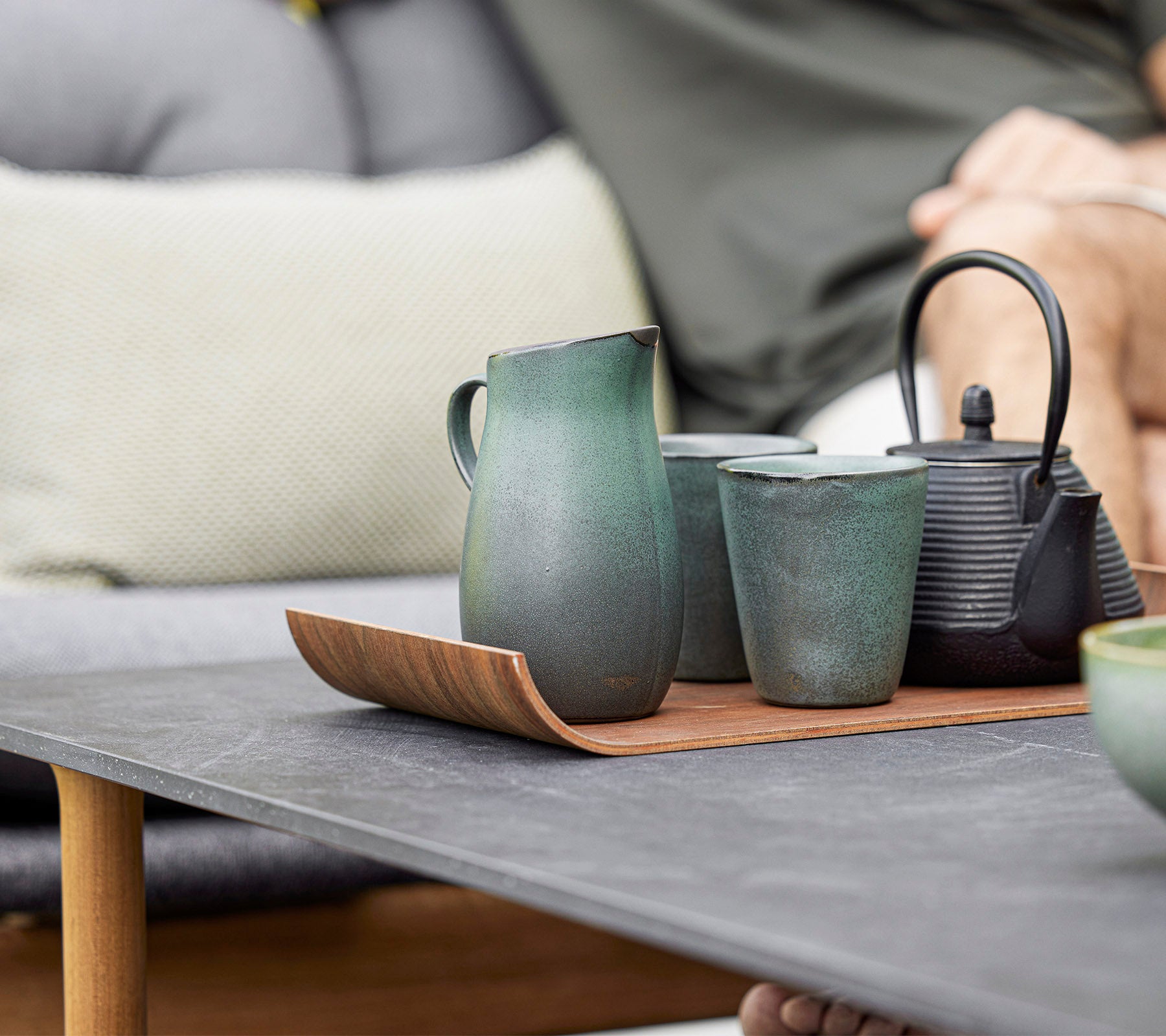 Una disposición elegante de tetera de cerámica, tazas y una jarra en una bandeja de madera, que muestra un diseño moderno y tonos terrenales.