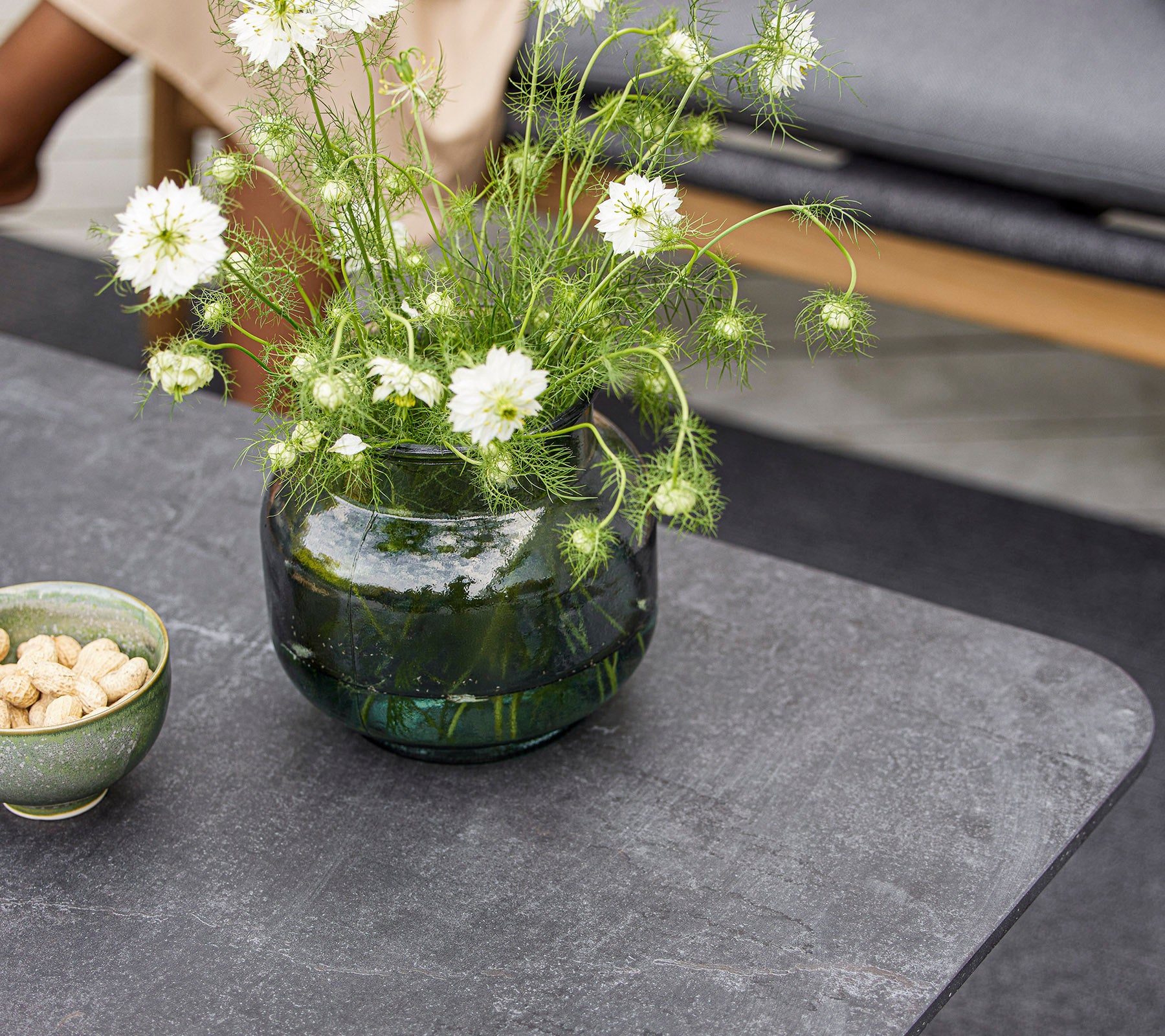 Una mesa moderna con un jarrón de vidrio redondo con flores blancas y un pequeño tazón de nueces. La superficie es lisa y texturizada.