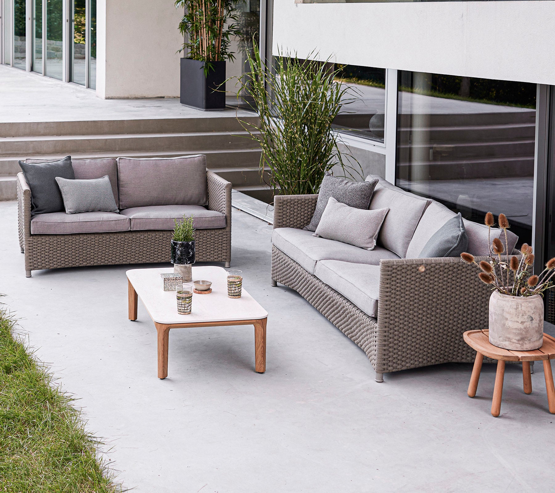 Disposición moderna de asientos al aire libre con un sofá, un loveseat y una mesa de café con elementos decorativos. Ambiente elegante y acogedor.