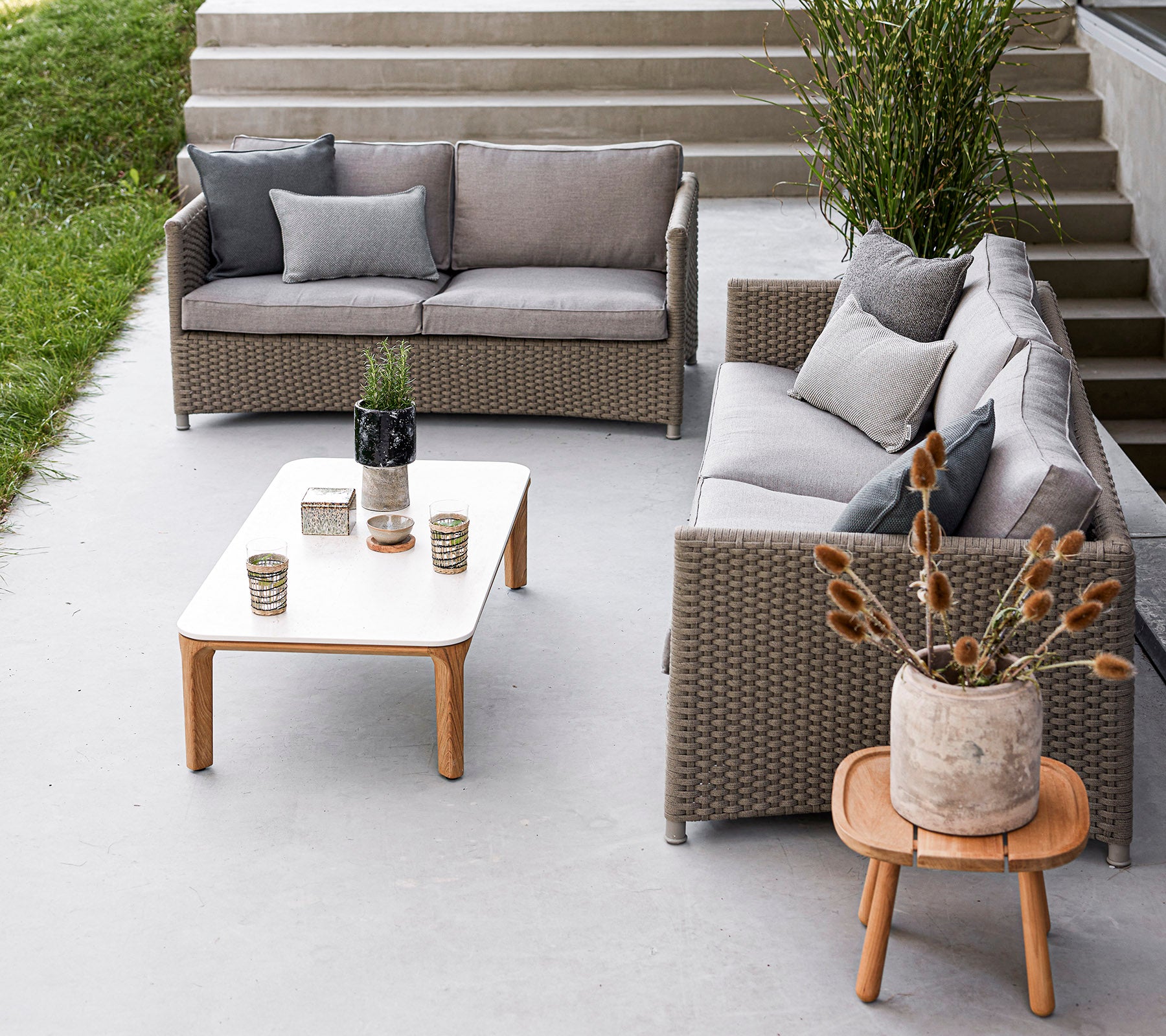 Acomodación de asientos al aire libre elegante con un juego de sofás gris, una mesa de madera, jarrones decorativos y plantas en macetas. Ideal para relajarse.