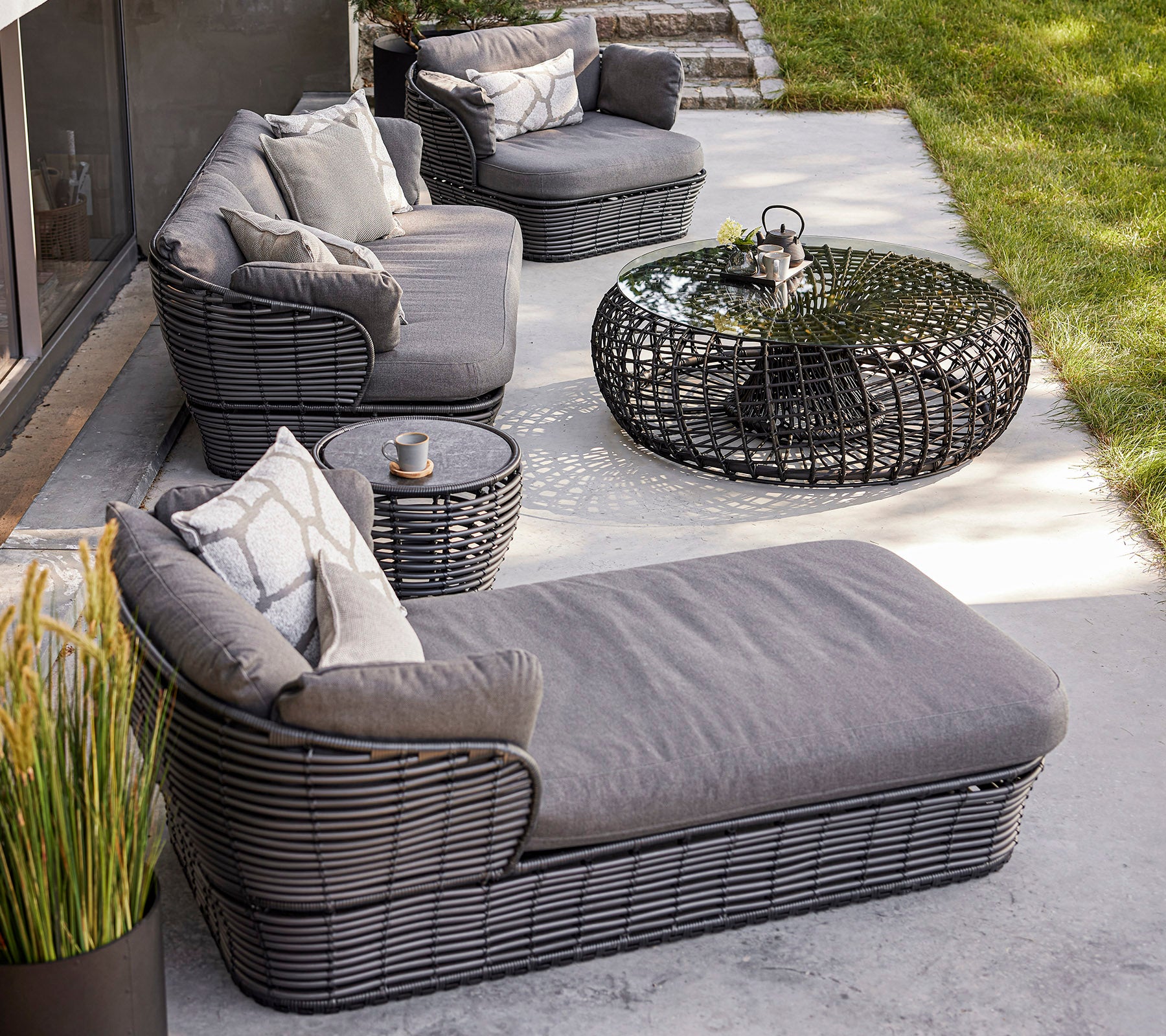 Arreglo de asientos al aire libre elegante con muebles trenzados, cojines, una mesa de café de vidrio y plantas decorativas. Ideal para relajarse.