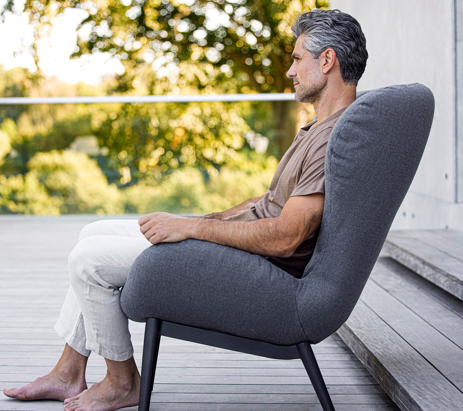 Hombre sentado cómodamente en una silla moderna con un diseño elegante, que muestra un tapizado suave y una forma minimalista y elegante.