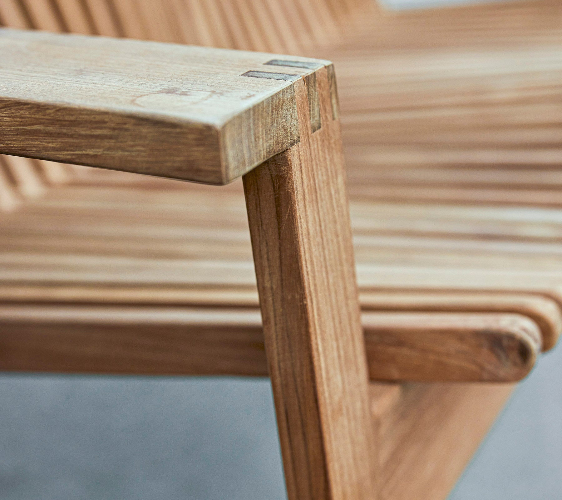 Primer plano de un reposabrazos de silla de madera que muestra un diseño elegante con asiento de tablones y acabados suaves.
