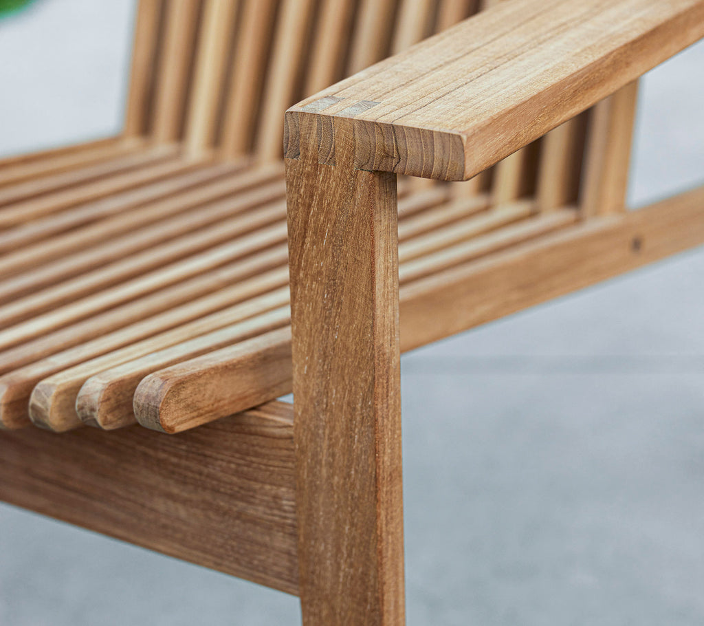Primer plano de un banco de madera con un diseño de listones y un reposabrazos resistente, mostrando la veta natural de la madera y la artesanía.