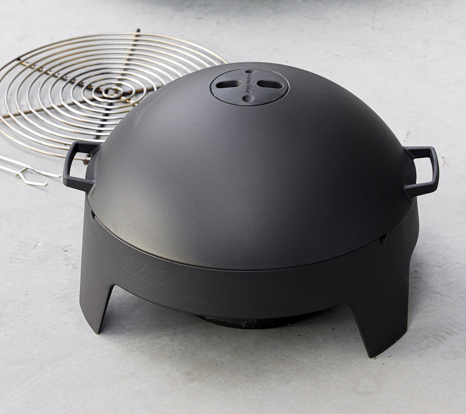 Un elegante electrodoméstico negro con forma de cúpula y asas, acompañado de una parrilla circular. Ideal para asar y cocinar al aire libre.