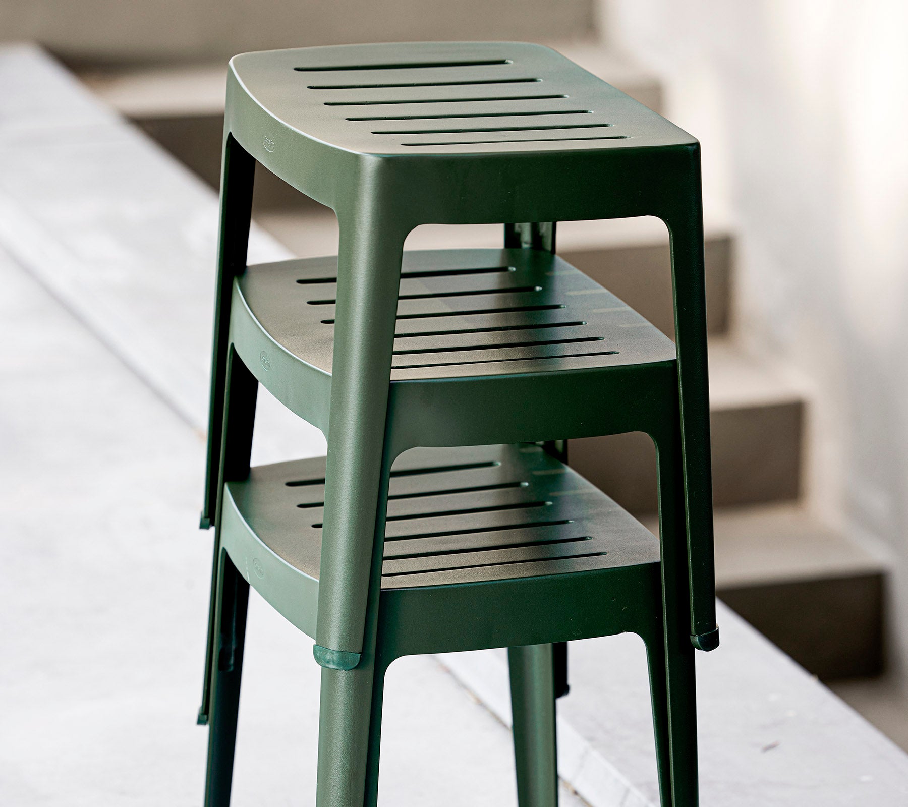 Taburetes de plástico verde apilables con asientos ranurados, diseñados para un uso informal. Ideales para arreglos de asientos versátiles.