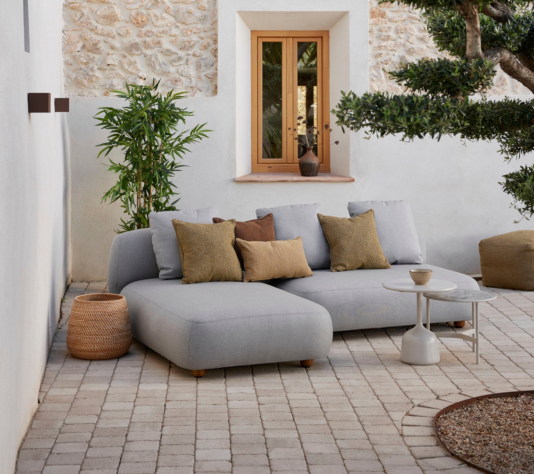 Sofá modular gris moderno con cojines decorativas, mesa auxiliar pequeña y elementos naturales en un ambiente acogedor.