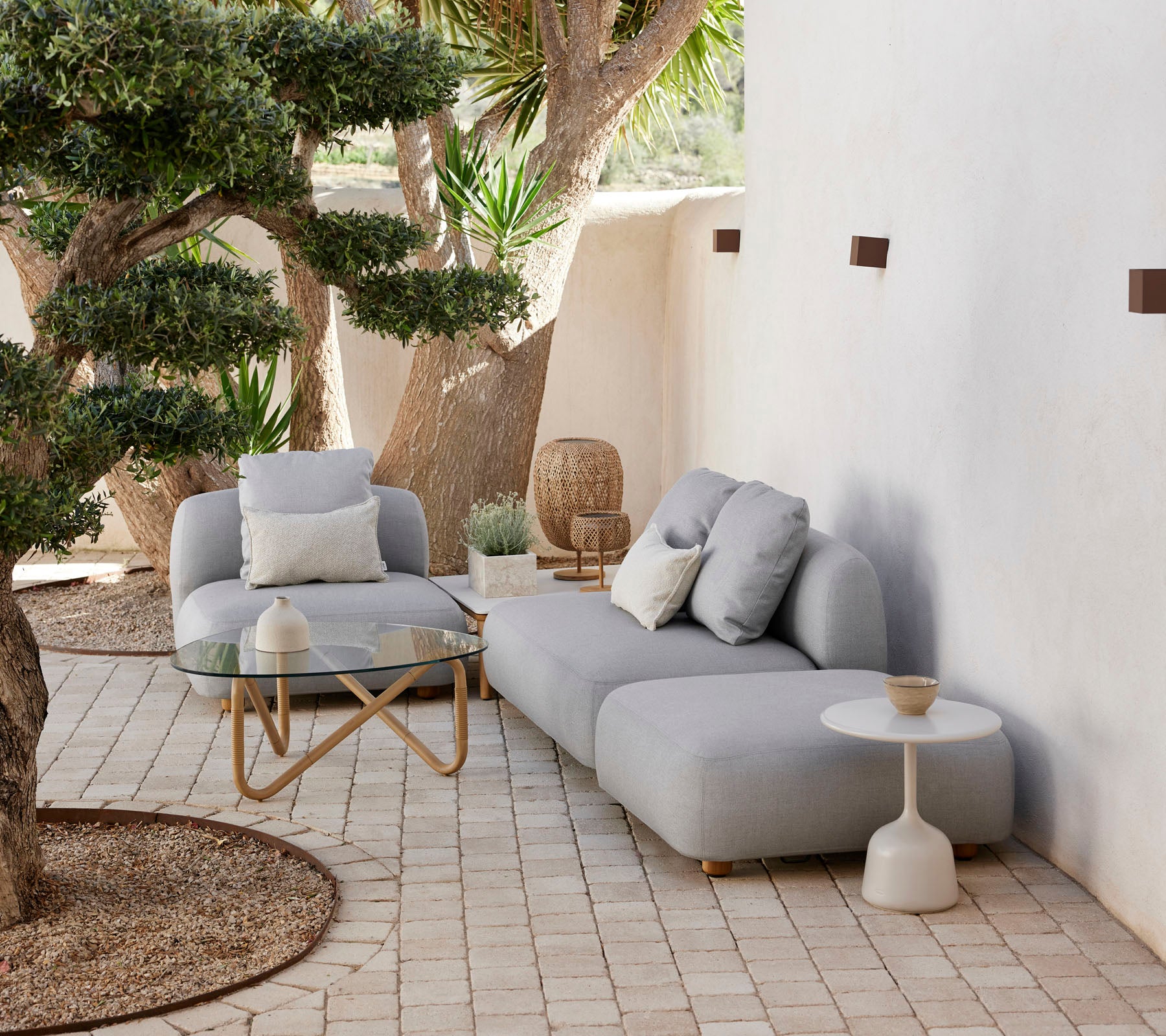 Conjunto moderno de asientos al aire libre con un sofá acogedor, una silla de acento y una mesa auxiliar estilosa, rodeado de vegetación y elementos decorativos.