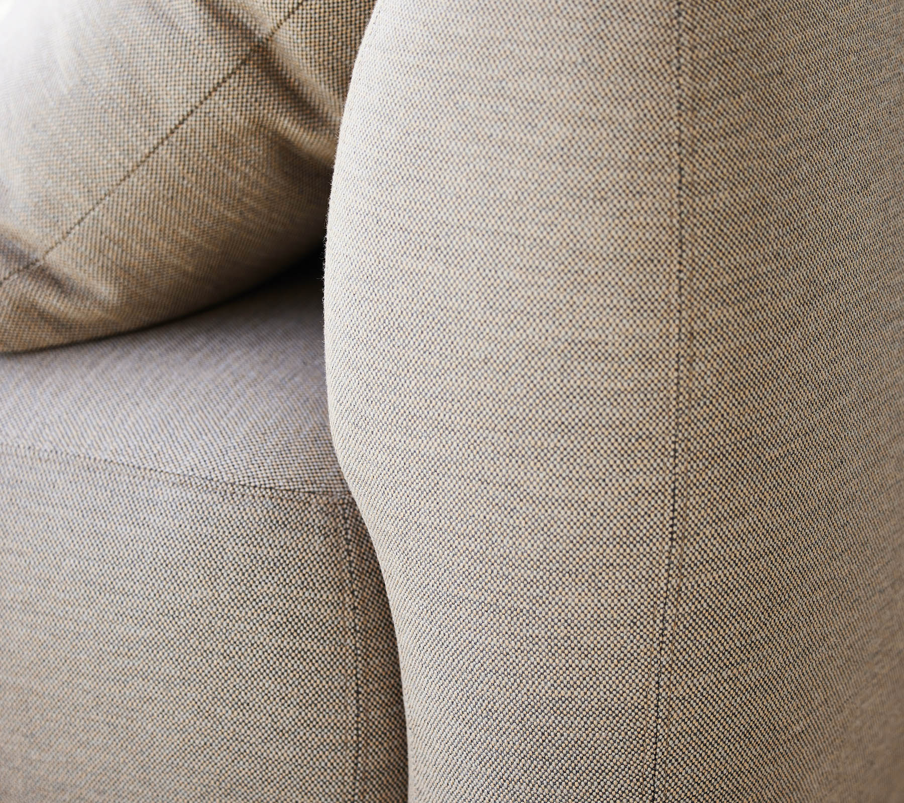 Acercamiento de un tapizado beige texturizado, destacando el reposabrazos curvado y los suaves cojines de una pieza de mobiliario.