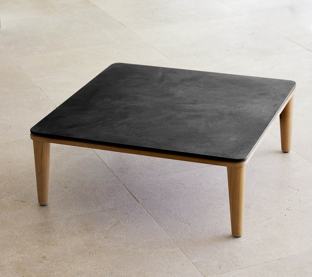 Mesa negra cuadrada con patas de madera en un entorno minimalista.
